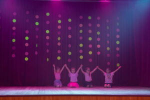 mākslas vingrotājas ar paceltām rokās sēž uz skatuves