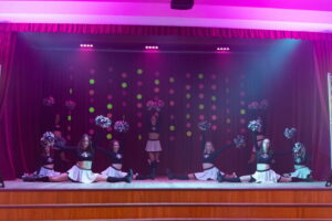 karsējmeitenes uz skatuves taisa špagatus ar pušķiem rokās